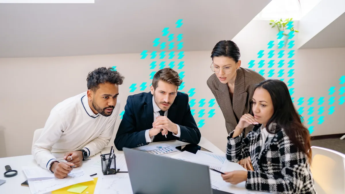 Equipe reunida diante de um notebook e de relatórios impressos